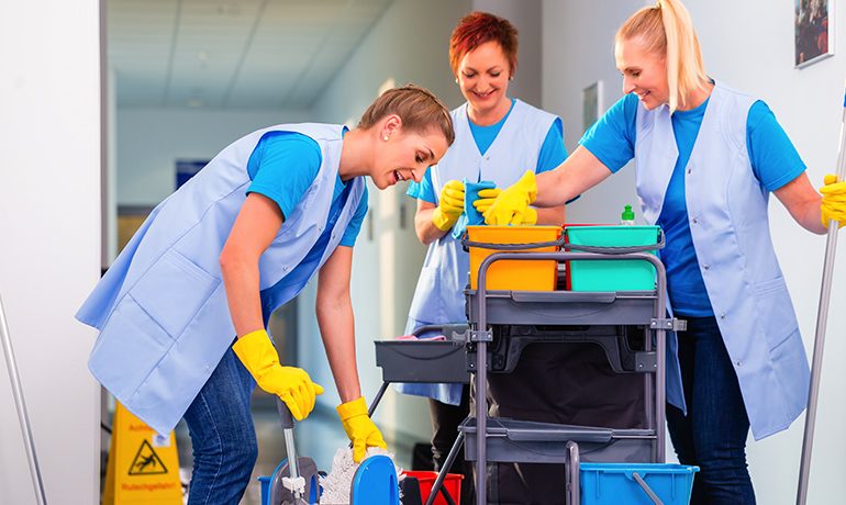 Drie schoonmaakmedewerkers werken met een schoonmaakwagen in een gang